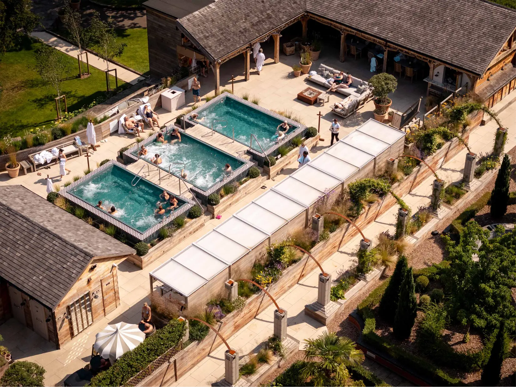 Aerial view of the spa terrace, outdoor pool, surrounding gardens, and mature woodland.