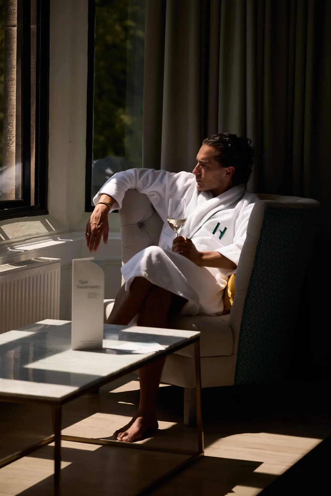 Guests relaxing in spa robes with drinks beside floor-to-ceiling windows overlooking the countryside at Eden Hall Day Spa.