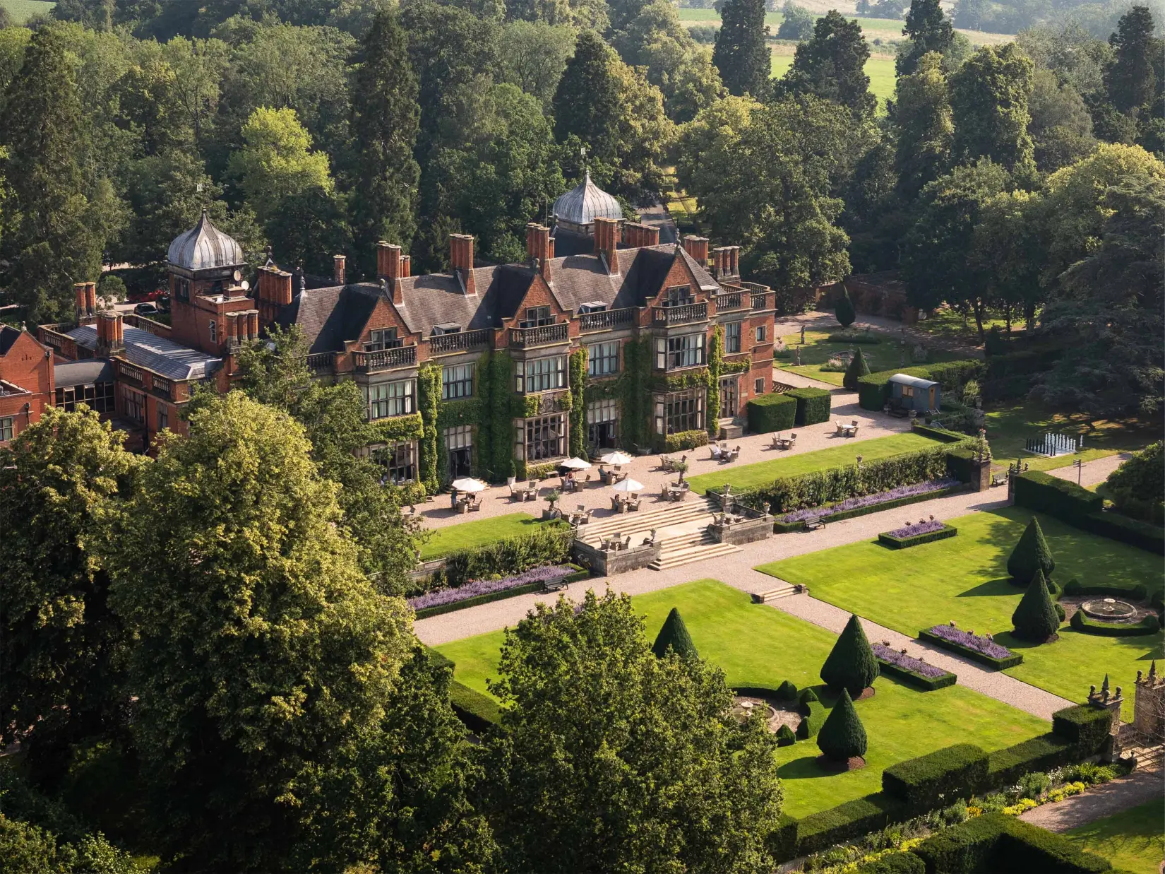 Formal landscaped gardens featuring manicured hedges, lawns, ornamental planting, and mature trees surrounding the country estate.
